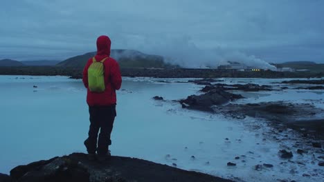 iceland, blue lagoon at night, svartsengi power plant, one person walking around the blue water, camera movement, camera follow tracking - dolly in on a steadicam gimbal stabiliser, wide angle lens