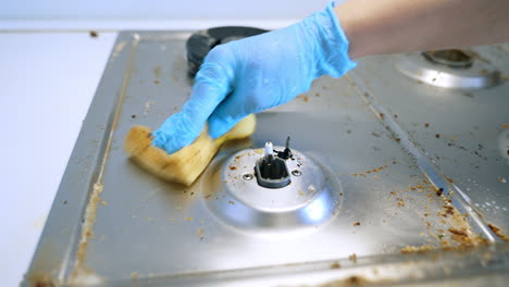 cleaning a stove top in a kitchen. a person in blue gloves cleans a dirty stove top in a kitchen, removing grease and food residue effectively