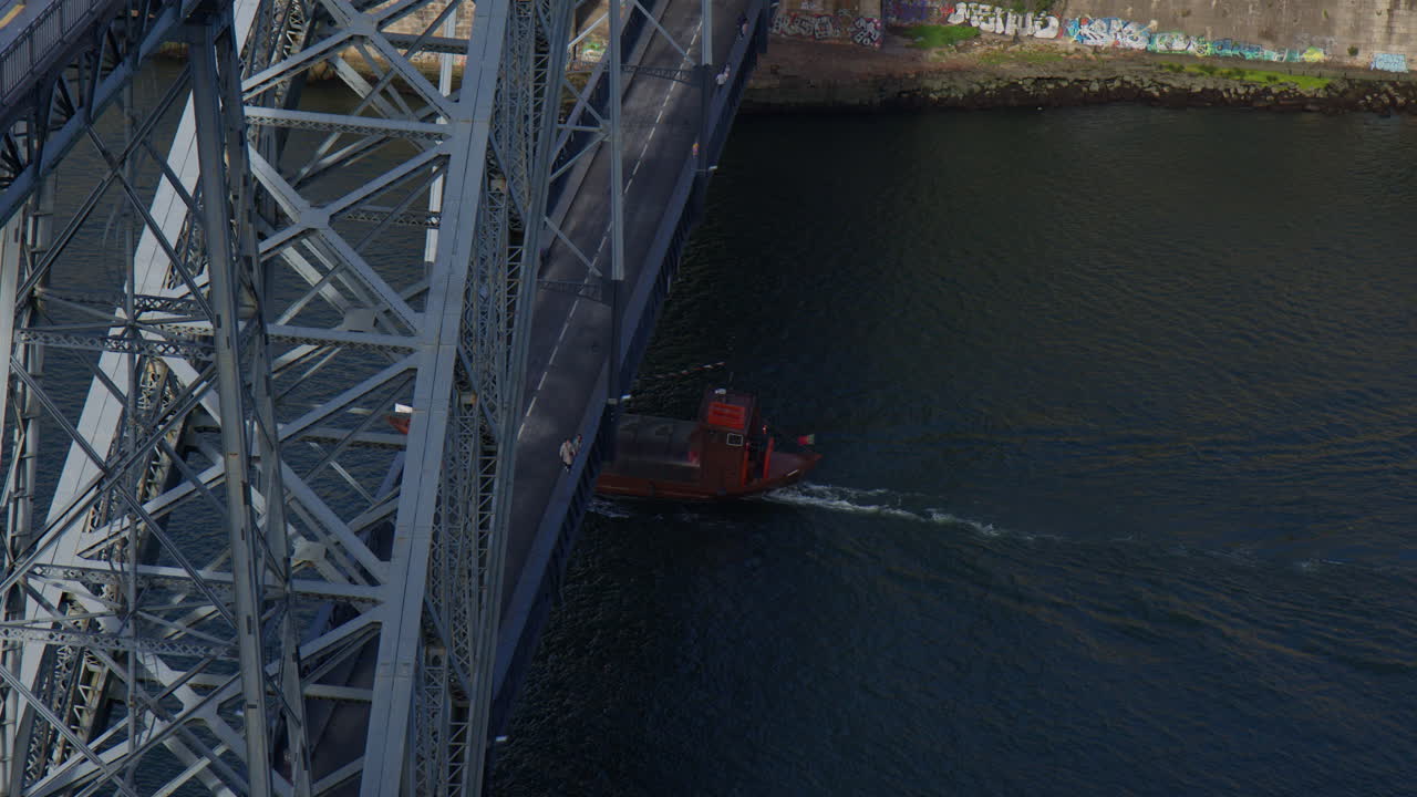 Traditional Boat Sailing Under The Dom Luis I Bridge On Douro River In Porto, Portugal. high angle shot, slow motion