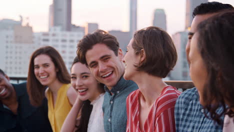 friends standing in a line gathered on rooftop terrace for party with city skyline in background