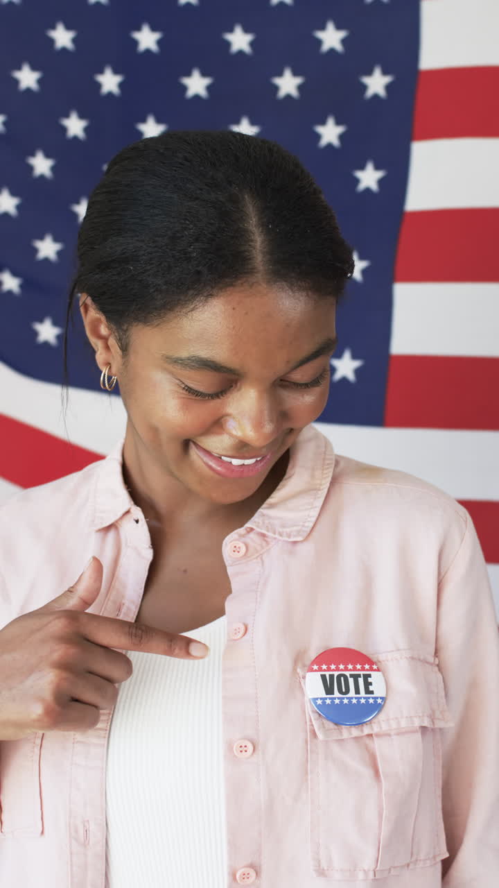 Vertical video: Smiling woman pointing at vote badge with American flag in background