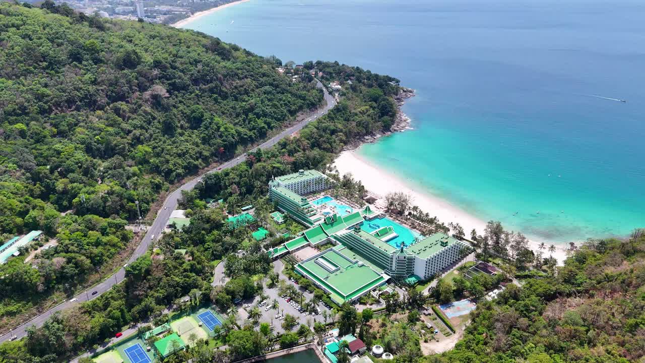 드론 영상은 태국 푸켓의 순수한 해변에 있는 럭셔리 호텔을 포착하여 울창한 초록색과 푸르키즈색 물을 보여줍니다.