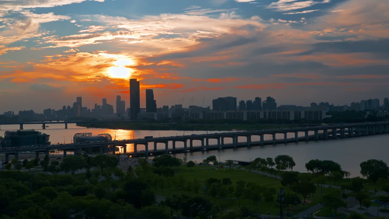 Intense sun setting behind Seoul skyline with Banpo Bridge and Han River park in foreground, skyscraper silhouettes and golden light reflected in water