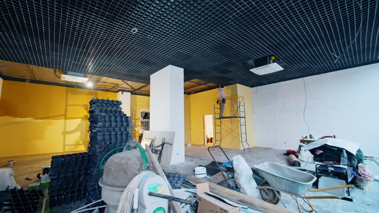 Large spacious room with building equipment, materials and devices. Builders' team work in the room finishing its mending.