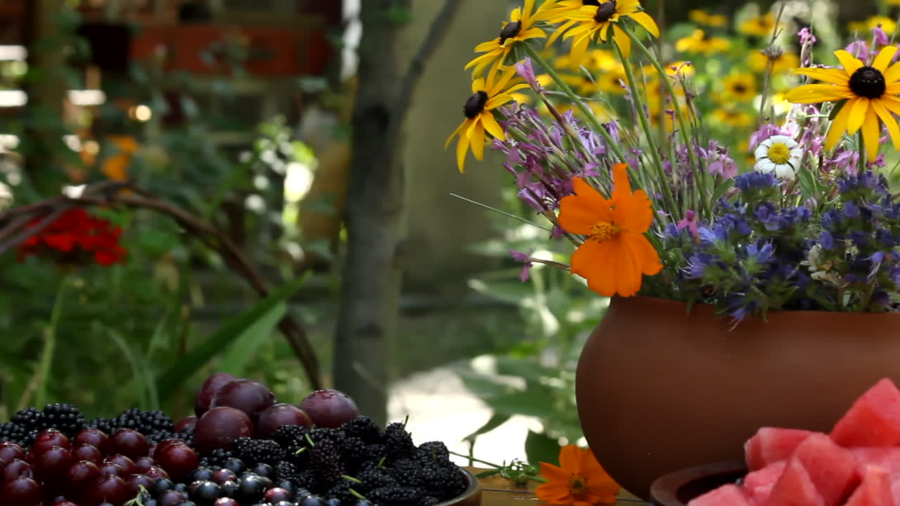 Cesto di uva fresca su tavolo con un bouquet di fiori autunnali in un vaso da giardino soleggiato.