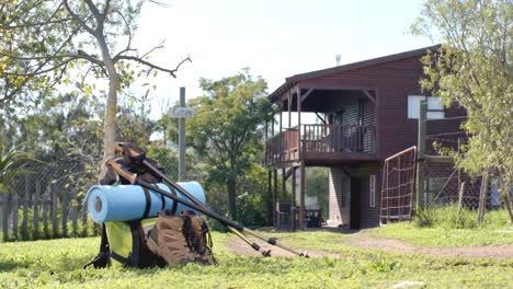 hiking shoes, sticks, mat and backpack lying on grass at log cabin, slow motion