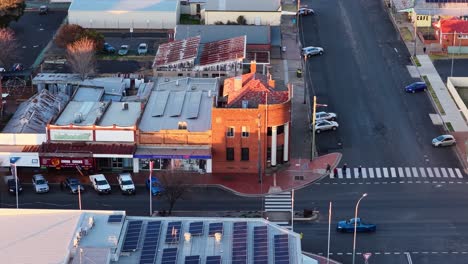 aerial camera glides over a quiet town street lined with historic buildings and parked cars, illuminated by warm sunset light, revealing urban layout