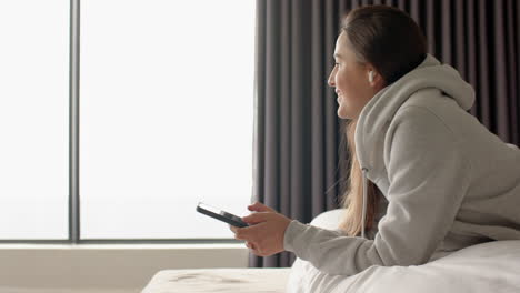 relaxing at home, woman holding smartphone and smiling while sitting on bed, copy space