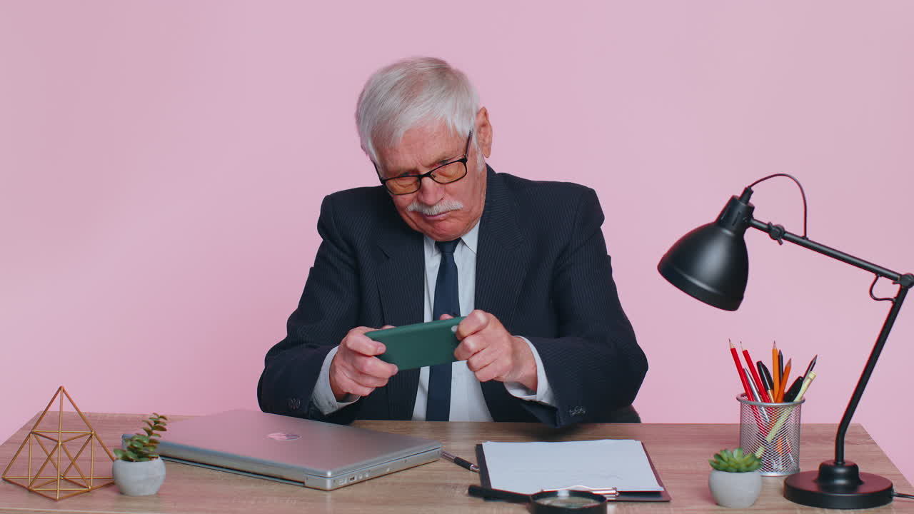 걱정스러운 고위 사업가 직장에서 앉아 일하는 것을 피하고 경주 또는 슈팅 비디오 게임을합니다.