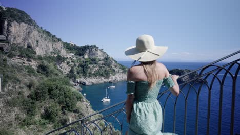 attractive caucasian woman in summer dress with hat, walking down the stairs with amazing coastal view on a nice sunny day in italy