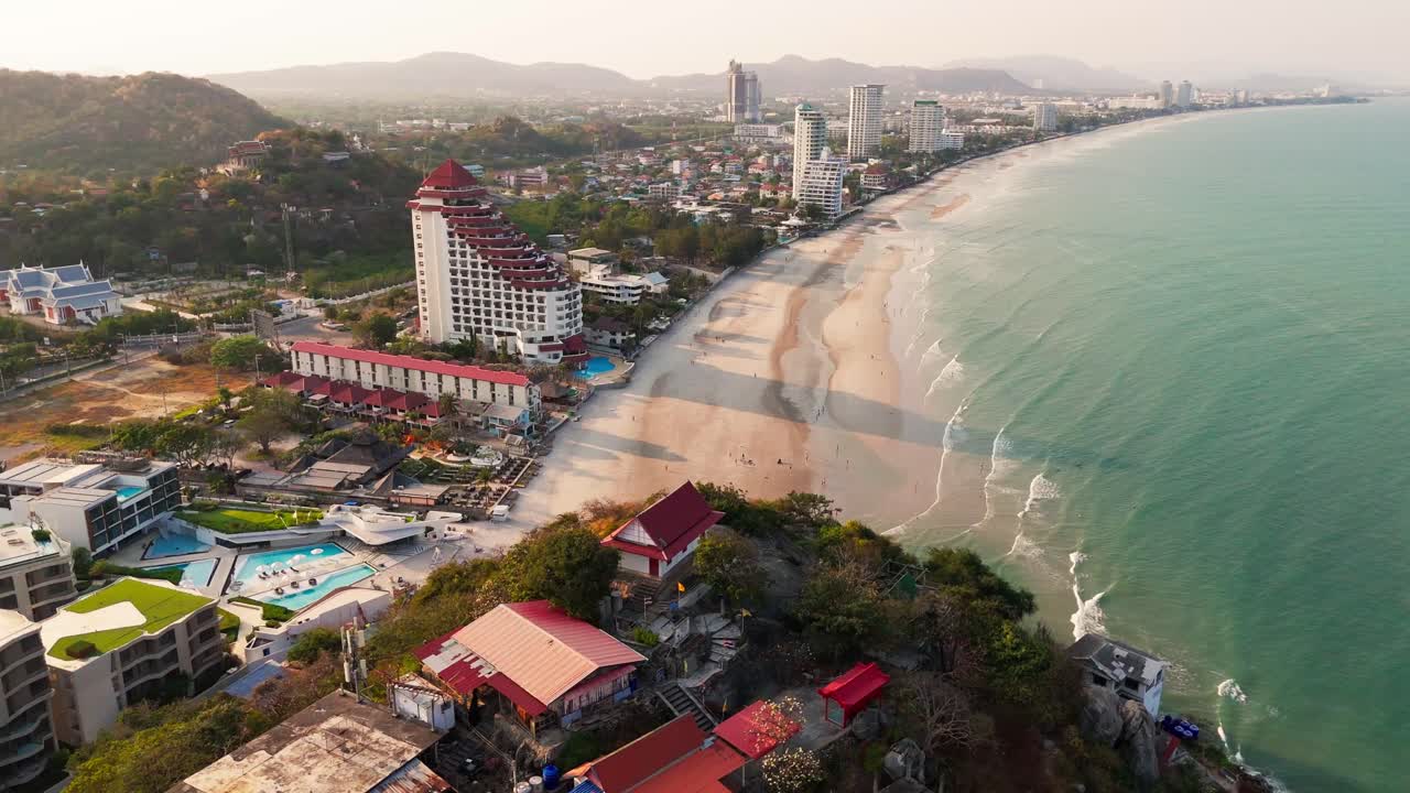 Vista aérea de Hua Hin en la playa durante el atardecer, dron volando sobre el agua del mar con un complejo hotelero rascacielos frente al mar