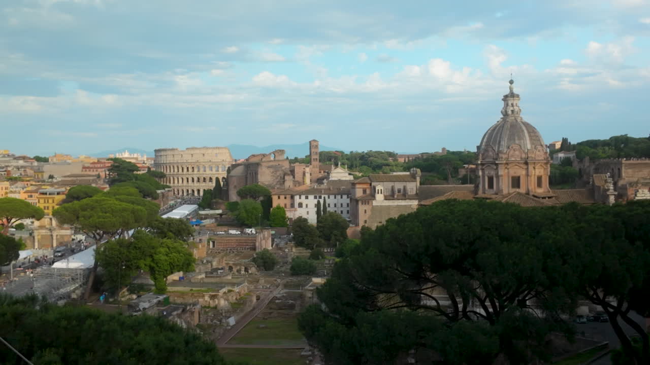 Panoramic view of central Rome with Colosseum, domes, and ancient ruins surrounded by lush trees.