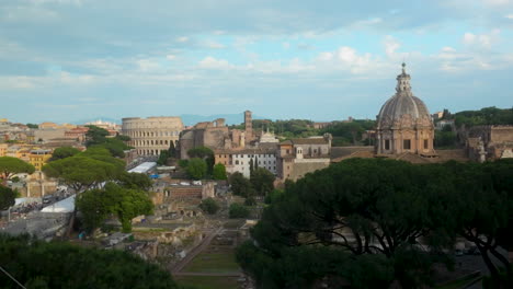 panoramic view of central rome with colosseum, domes, and ancient ruins surrounded by lush trees.