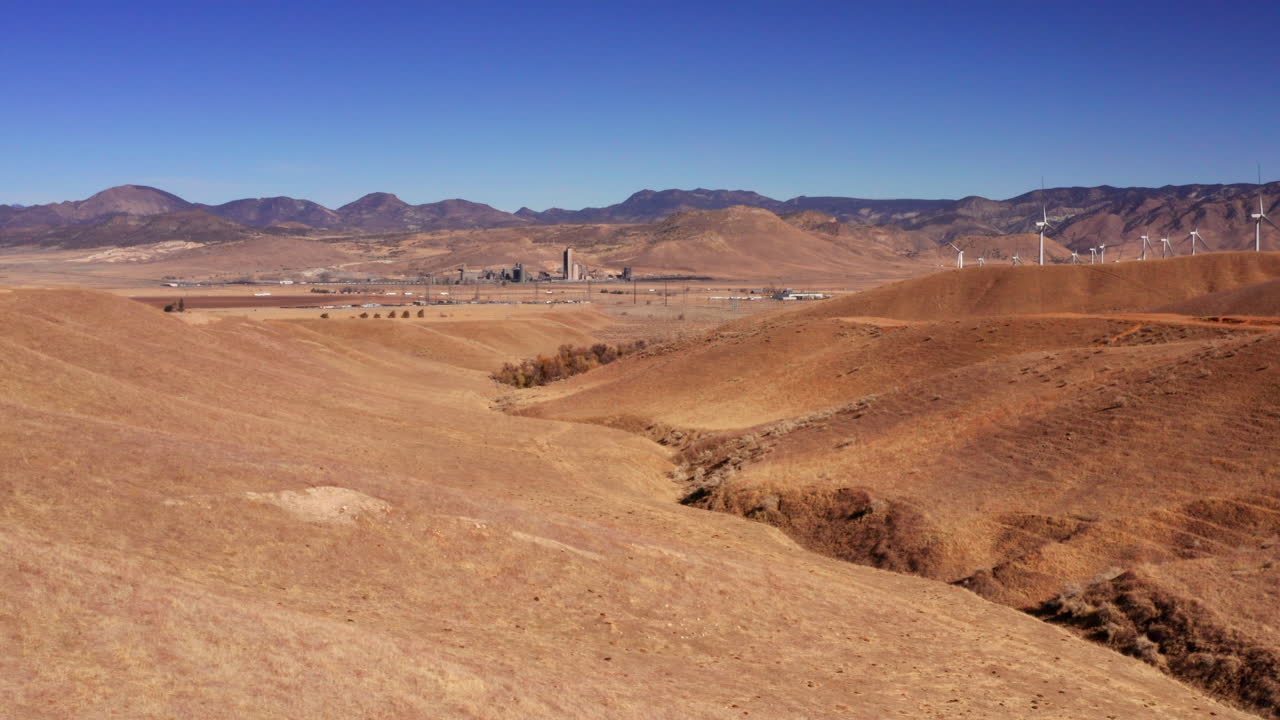 colinas onduladas de pastizales secos con turbinas de viento en la ladera y granjas y un granero en las tierras de cultivo distantes - vista aérea