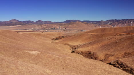 Colinas-Onduladas-De-Pastizales-Secos-Con-Turbinas-De-Viento-En-La-Ladera-Y-Granjas-Y-Un-Granero-En-Las-Tierras-De-Cultivo-Distantes---Vista-Aérea