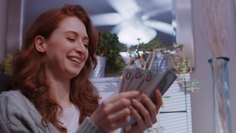 -A-young-caucasian-woman-is-sitting-at-home-counting-money,-happy