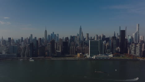 Aerial-ascending-shot-of-modern-metropolitan-city.-River-and-downtown-skyscrapers-on-sunny-day.-Manhattan,-New-York-City,-USA