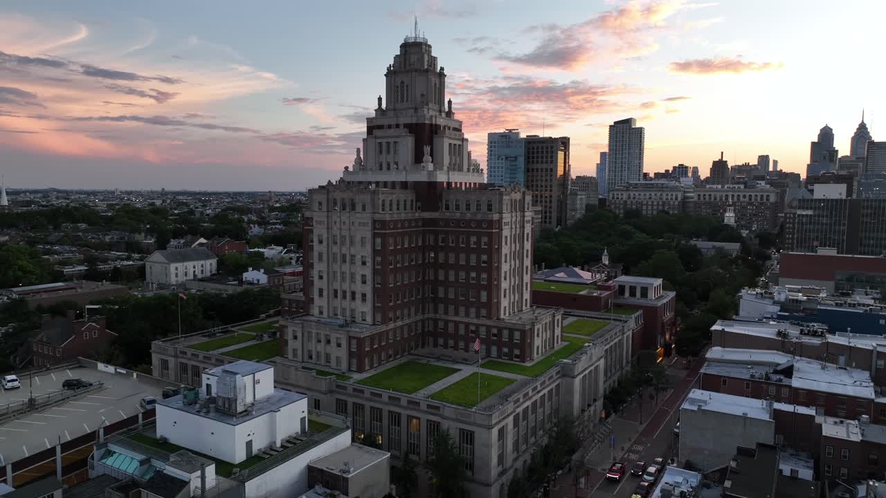 The United States Custom House at Sunset time in Philadelphia, PA. Aerial wide shot. Waving American flag and skyline skyscrapers of downtown in back. Metropolis of USA