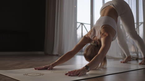 allenamento yoga in una sala con grandi finestre e luce solare che passa attraverso il telaio. una donna in abiti sportivi bianchi si allena in palestra su un tappetino