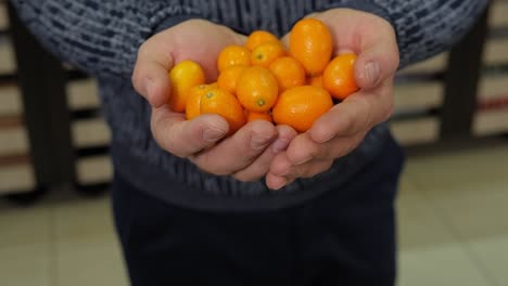 close-up of a man holding a kumquat in a grocery store.