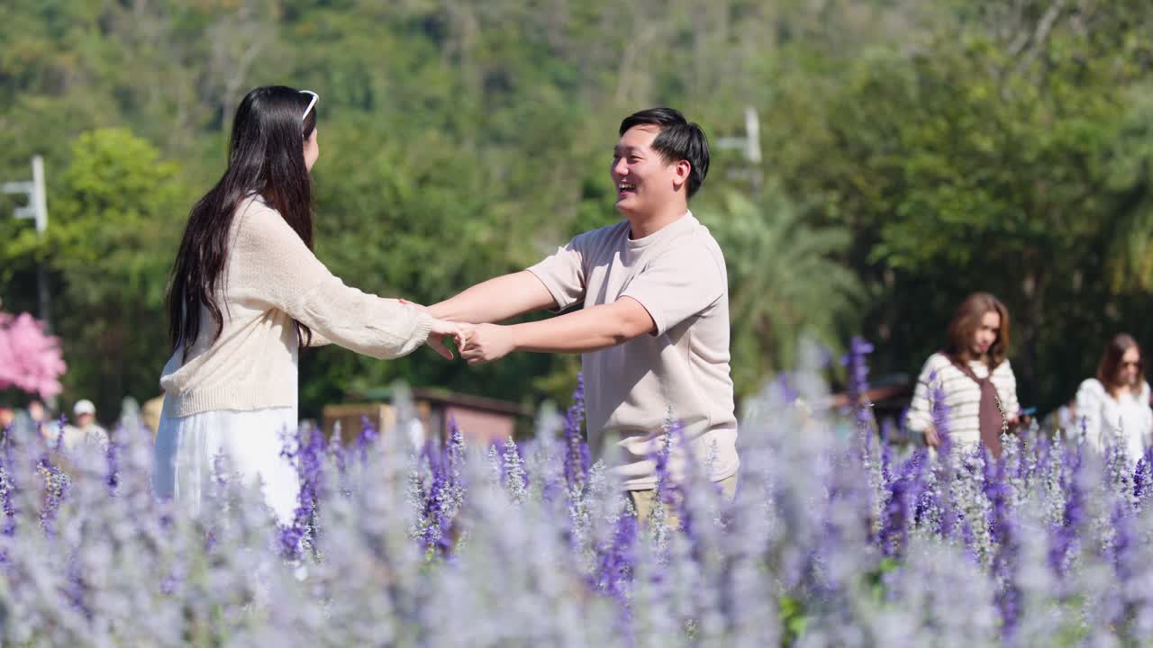 부드러운 배경 블러 효과가 있는 화창한 보라색 꽃밭에서 미소를 지으며 장난스럽게 손을 잡고 있는 커플