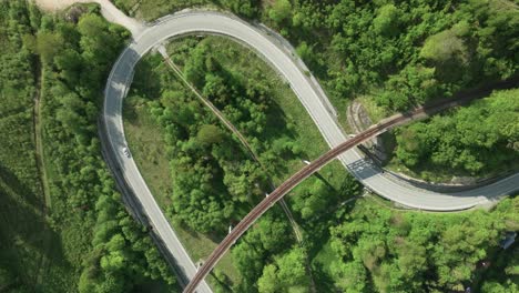 static aerial overhead view of a winding road intersected by an old railway bridge in the middle of a forest