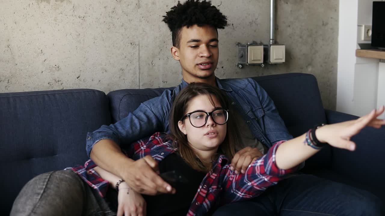una pareja feliz de jóvenes hipsters lindos acostados en el sofá, tratando de encontrar el canal de tv perfecto. tiempo libre, disfrutando de la juventud, viviendo juntos. metas de relación.