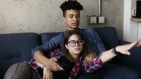 cute happy couple of young hipsters lying on the couch, trying to find a perfect tv channel. leisure time, enjoying youth, living together. relationship goals.