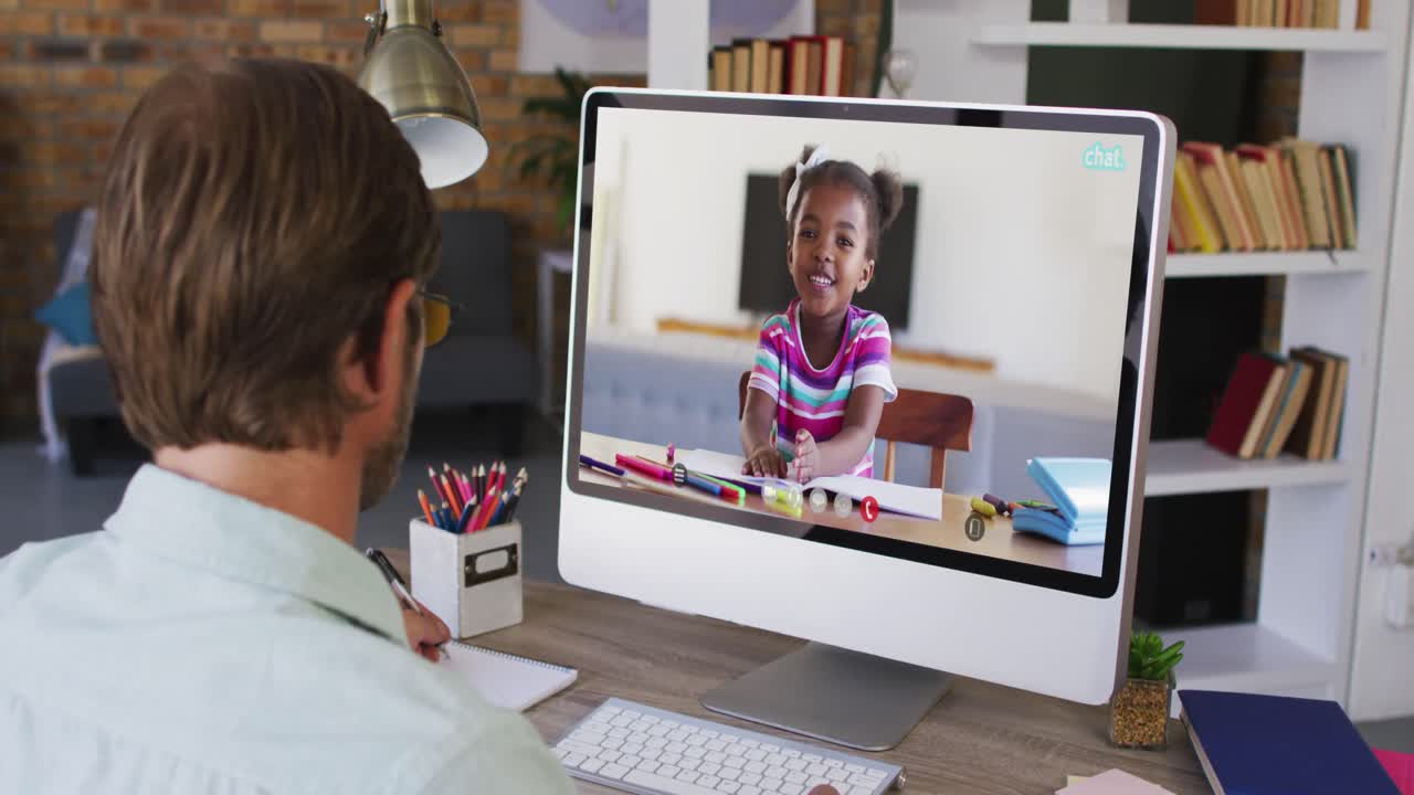 Ein kaukasischer Lehrer macht Notizen, während er einen Videoanruf mit einem afrikanisch-amerikanischen Mädchen am Computer führt.