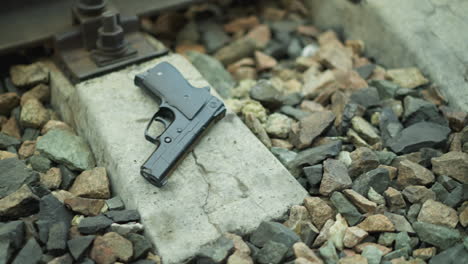 a close view of a handgun placed on the concrete base of a railway track surrounded by rocks, with a blurred background