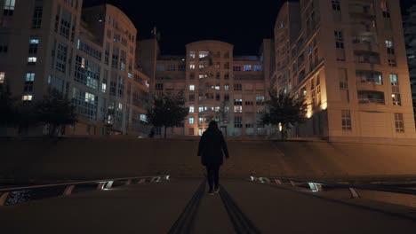 low angle shot : the girl is on the small bridge and approaching l'arbre blanc at night, montpellier - france