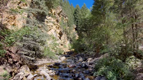 Mountain-Valley-Stream-below-rugged-cliffs---aerial-pull-back-in-slow-motion