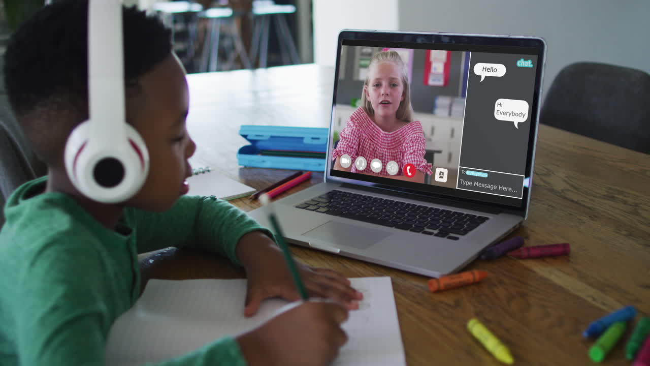 Schoolboy using laptop for online lesson at home, with schoolgirl talking and web chat on screen