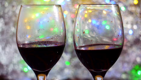 dos copas de vino vino tinto sentado en un bokeh colorido en movimiento y una manta plateada de cerca en un ambiente íntimo y romántico
