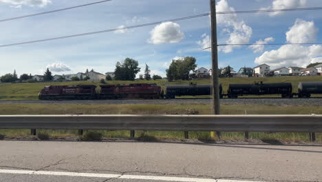 oil tanker train traveling alongside highway on sunny day. real time, dolly left, passenger pov