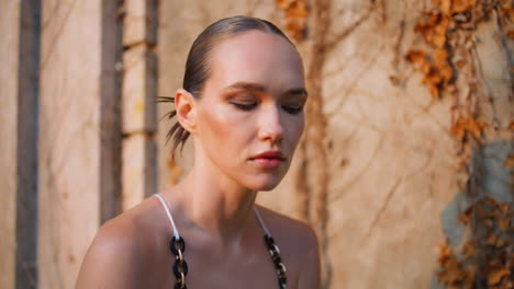 fashion model posing sunlight in front old wall covered dry leaves close up.