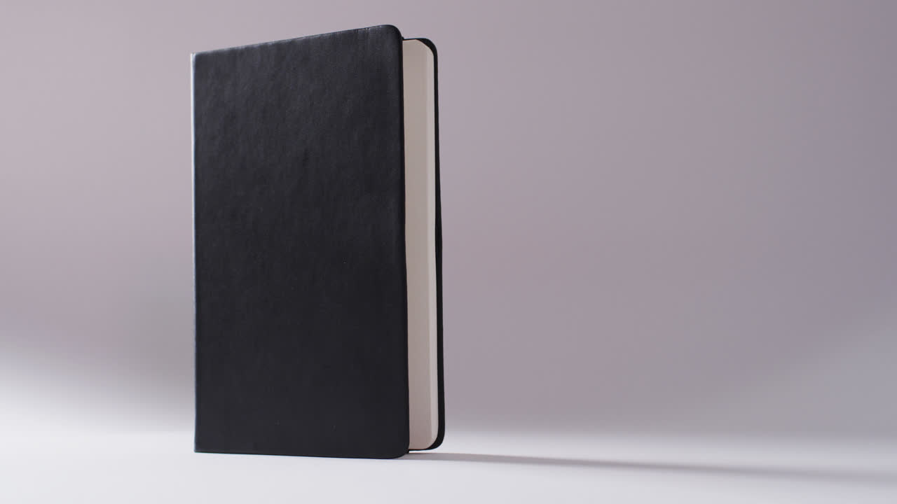 Close up of open black book standing vertical with copy space on white background in slow motion