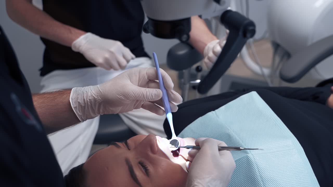 Dentist examines patient's teeth through the microscope. Specialist looks into female's mouth with medical tools in a dental office.