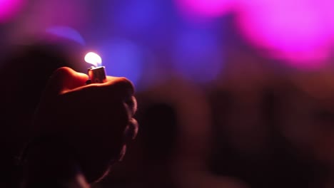 Close-up-shot-of-a-hand-with-a-lighter-sticking-out-of-a-crowd-during-a-concert-with-colorful-background-in-blurred-view