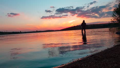 a woman catching fish in a calm lake just after a spectacular sunset