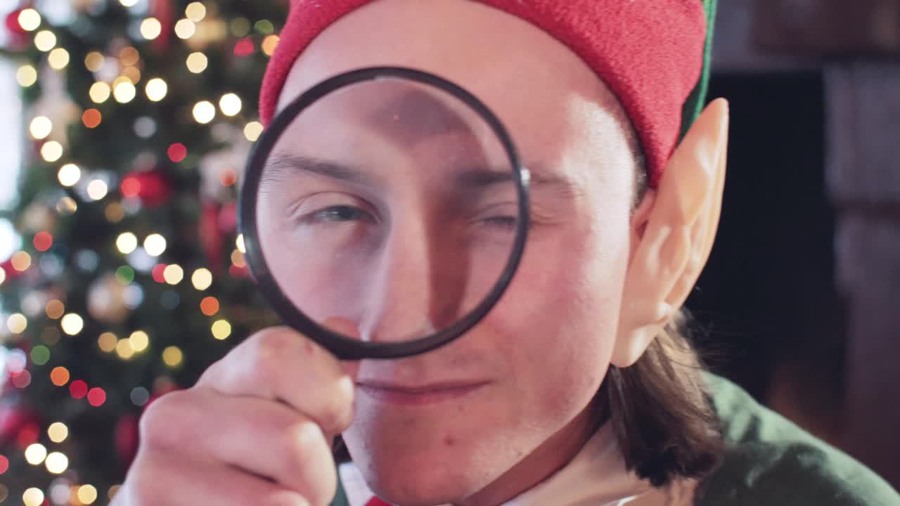 Elf boy is played with a magnifying glass in the room near the Christmas tree