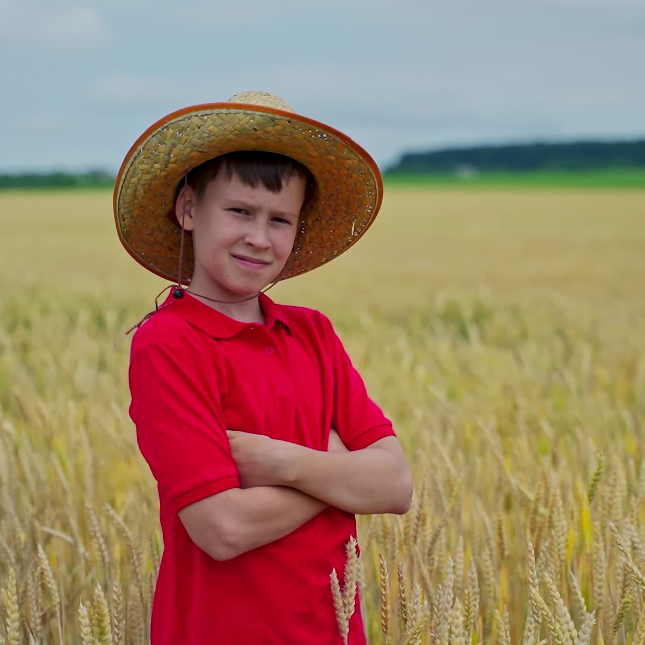 Portrait of a little farmer on field. Serious boy in straw hat standing on the golden field in summer day. Agriculture and summer vacation.