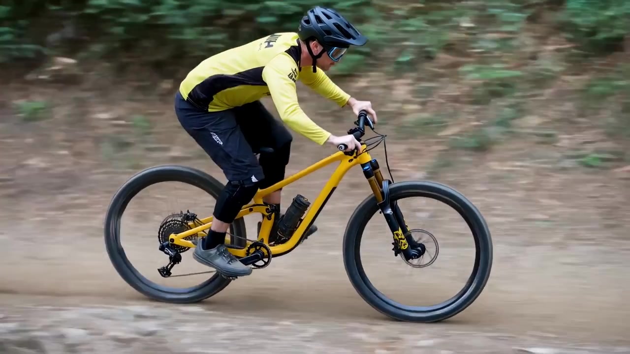 Ciclista in sella vicino alle radici, che sposta il peso, assorbendo gli urti su un sentiero sterrato, maglia gialla, batteria.
