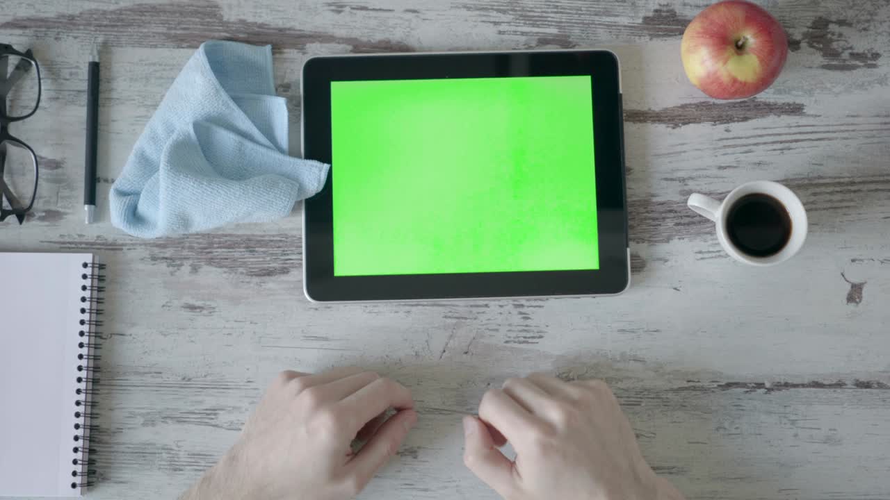 Hands holding tablet pc with green empty screen on wooden background