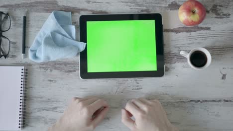 manos sosteniendo tableta pc con pantalla verde vacía en fondo de madera