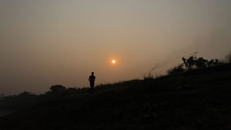 Establisher-shot-of-silhouetted-runner-jogging-towards-camera,-sunset-sun-behind