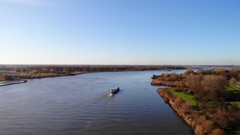 Luftaufnahme-über-Die-Herbstliche-Landschaft-Neben-Der-Oude-Maas-Mit-Vorbeifahrendem-Schiff-Im-Hintergrund