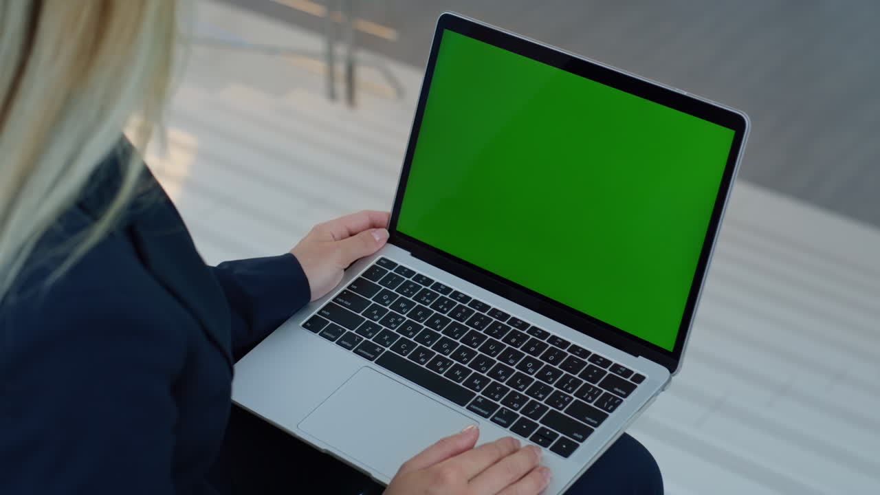 Businesswoman holding laptop green screen display on knees indoors closeup