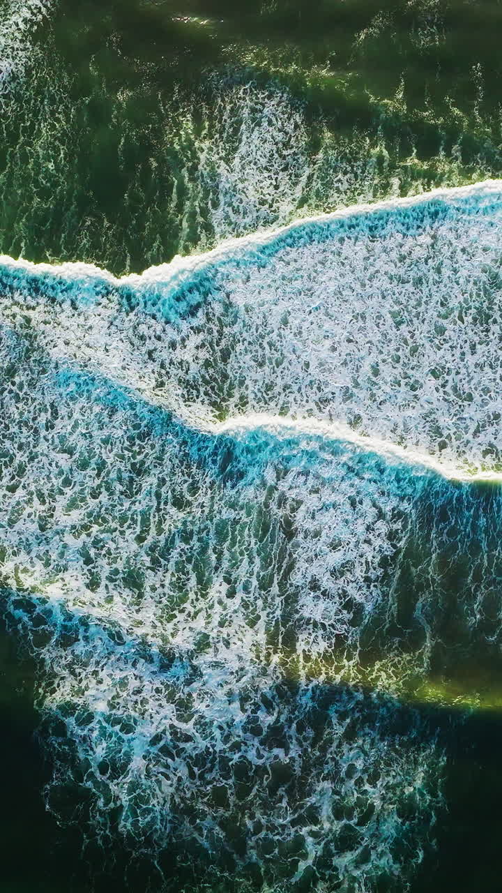 Beautiful relaxing movement of foamy waves on the surface of ocean. Descending drone footage over the deep green waters. Vertical video