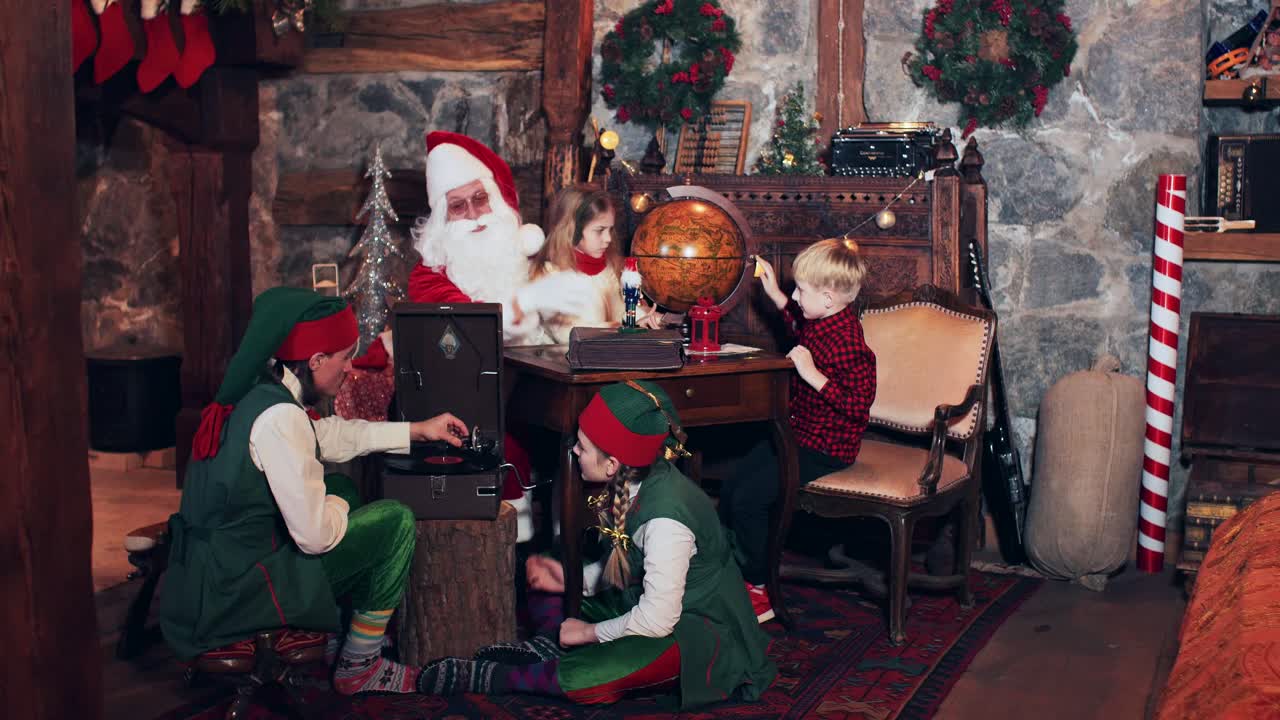 A boy and a girl, together with Santa, are exploring countries on an old globe. Christmas elves near the fireplace listening to a retro gramophone